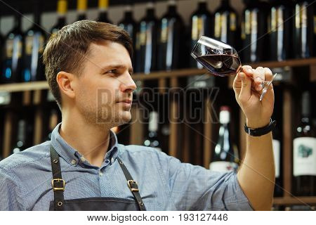 Bokal of red wine on background of male sommelier appreciating color, quality, flavor and sediments of drink. Professional degustation expert in winemaking.