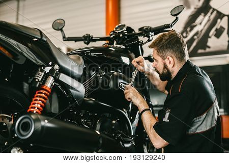 Professional mechanic working screwdriver and motorcycle repairs. Handsome young man repairing motorcycle in repair shop.