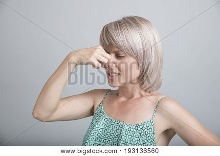 Female gesture smells bad. Portrait of woman wearing casually pinches nose with fingers hands looks with disgust something stinks bad smell situation. Human face expression body language reaction.