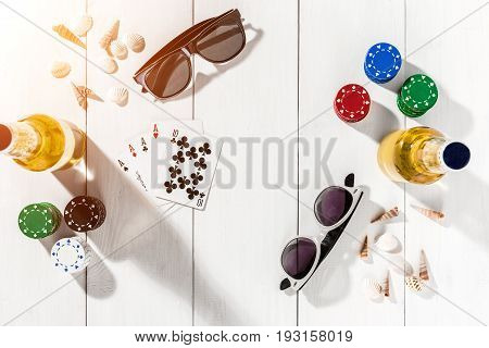 Gambling. Poker chips, cards and two bottles of beer on white wooden table. Top view. Copyspace. Poker. Summer. Sun flare