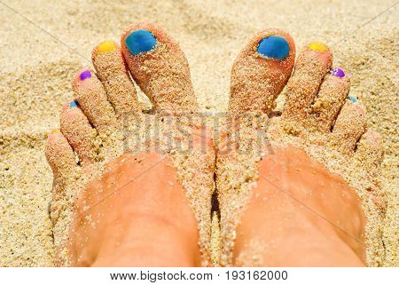 Women feets with colorful nails in the sand