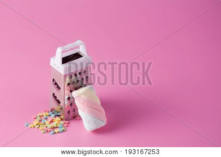 Grater and colorful marshmallow on pinck background