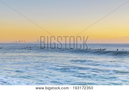 Colourful sunrise colours in the skies, with surfers wading in the ocean for the next waves. View from Currumbin Rock to Surfers Paradise, Gold Coast