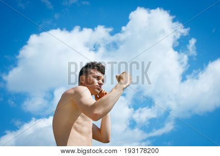 Beautiful athletic man with a naked torso striking against the blue sky and white clouds
