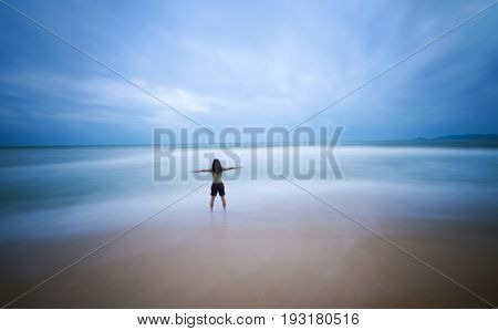 Long exposure motion blurred of rear view female open arms standing on a sea shore.