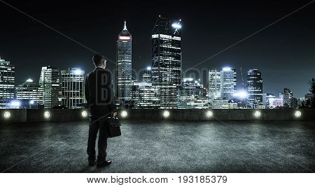 Businessman looking and thinking at roof top with modern city skyline background night scene .