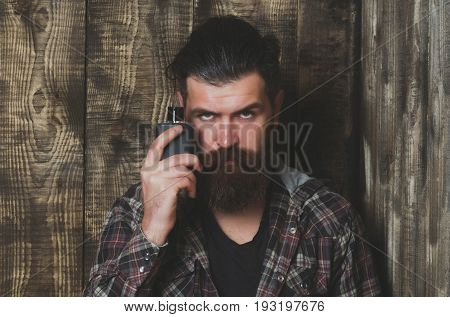 Bearded man or brutal caucasian hipster with grey hair long beard and moustache posing with black perfume or cologne bottle on wooden background. Male fragrance and perfumery. Cosmetics