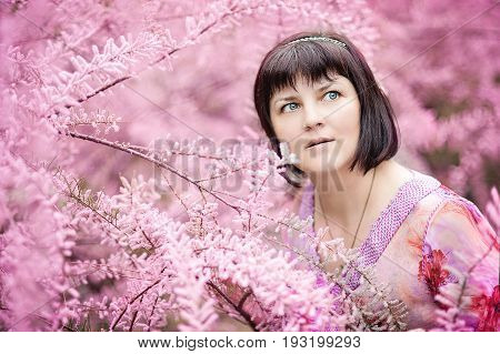 Portrait of a middle-aged woman in pink flowers of tamaricaceae. Beautiful romantic woman in Tamarix