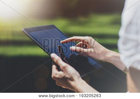 Hipster young girl using tablet or holding gadget planning travel plan. Female hands holding computer tourist traveler texting message on device on green background in Parc Laberint Barcelona. Mockup for text flare and bokeh