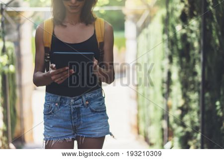 Hipster young girl with bright backpack and vintage camera using tablet or holding gadget planning travel plan. View tourist traveler on background Parc Laberint Barcelona. Mock up for text message