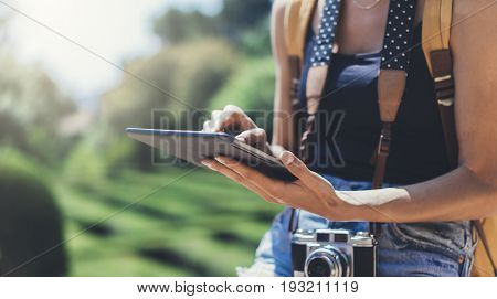 Hipster young girl with bright backpack and vintage camera using tablet or holding gadget planning travel plan. View tourist traveler on background Parc Laberint Barcelona. Mock up for text message