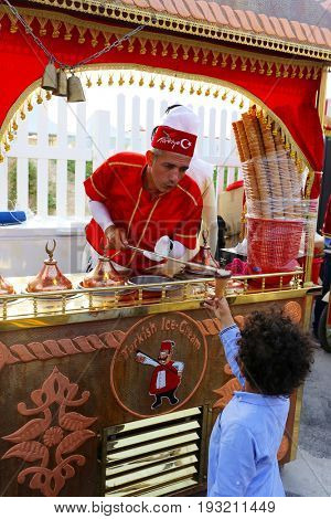 DOHA, QATAR - APRIL 8, 2017: A Turkish traditional ice-cream vendor demonstrates the dramatic process of filling a cone to an enthusiastic  customer at the Magical Festival Village near Katara, Doha.