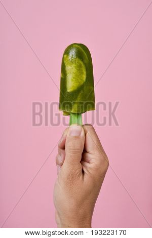closeup of a young caucasian man with a homemade mojito ice pop in his hand, against a pink background