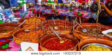 Colorful collection of homemade local Mexican food in clay pots arranged on market table.