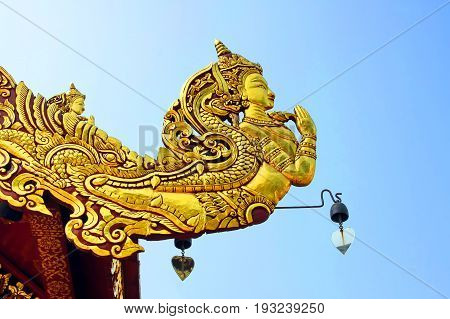 Native traditional Thai style angel carve on roof decoration and blue sky Golden Kinnaree act paying respect or sawasdee of Thailand The mythical half bird half woman