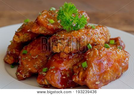 Barbecue chicken wings on white plate put on wood table. Homemade barbecue chicken wing delicious moist and spicy. Close up view of barbecue chicken wing decorated with spice and parsley on white plate ready to served.