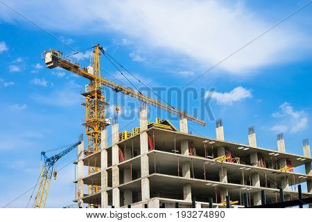 Yellow tower crane and building under construction against blue sky. Beautiful sky with clouds. Urban fabric of the city develops.