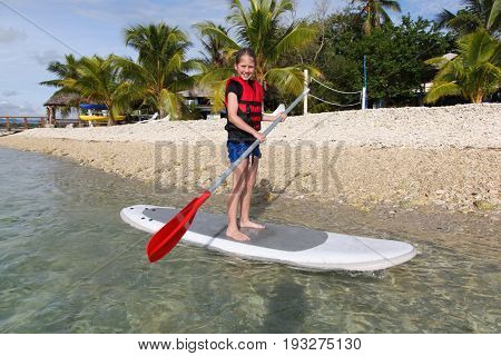 A young girl enjoying Stand Up Paddle Boarding in Vanuatu. Vanuatu is a popular tropical destination in the South Pacific