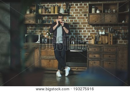 Serious Man Talking On Smartphone And Eating Apple At Home