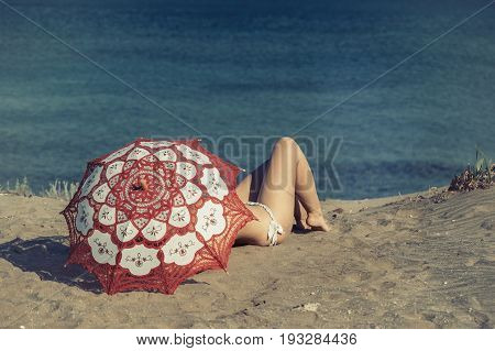 Beautiful naked female lies on the beach under a red umbrella. Girl on the sand under the umbrella