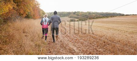 Pillar Box Format Shot Of Mature Couple Running Around Field