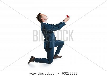 young man in suit standing on one knee and making marriage proposal isolated on white