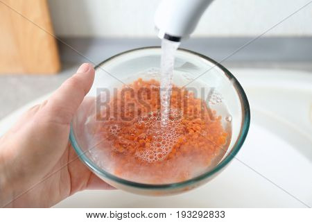 Hand of woman washing raw lentils with tap water before cooking in kitchen
