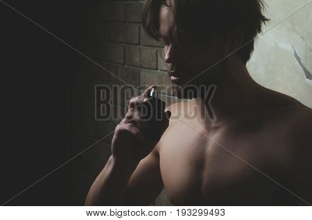 man or handsome unshaven macho with naked chest smelling perfume scent with closed eyes on dark background. Male fragrance and perfumery. Cosmetics beauty and spa copy space