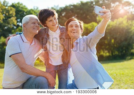 Now smile. Vibrant happy nice relatives posing for a photograph while the man using his smartphone for making a selfie