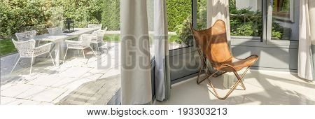 Glazed bay windows in orangery with a leather butterfly chair and view on the garden with furniture