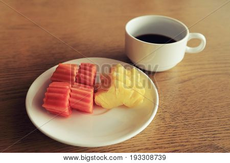 Diet set plate of fresh fruits with a cup of black coffee on wooden table background vintage toned color image.