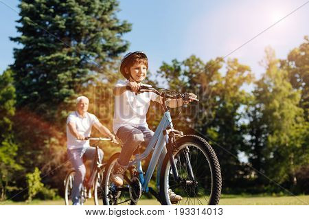 Healthy and fun. Bright sweet optimistic child enjoying his hobby while spending the day outdoors and riding bicycles with his grandpa
