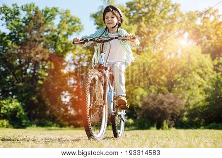 Determined to move forward. Adventurous active sweet boy feeling delighted while taking a ride on his bicycle and enjoying the warm weather