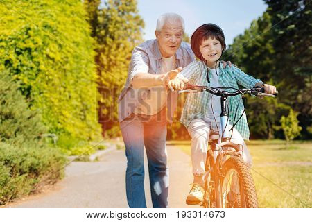 Look on the road. Friendly enthusiastic aged gentleman giving his grandchild a lesson on how riding a bike while spending the day with him