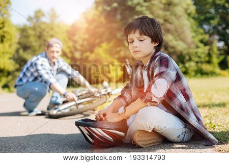 Dont be sad. Expressive joyless sweet child sitting on the road and waiting while his dad repairing the bicycle