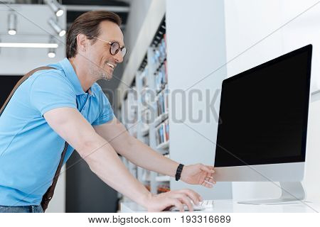I could scarcely believe my eyes. Happy man grinning widely and leaning on a display while eying a personal computer at showroom of an electronics store.