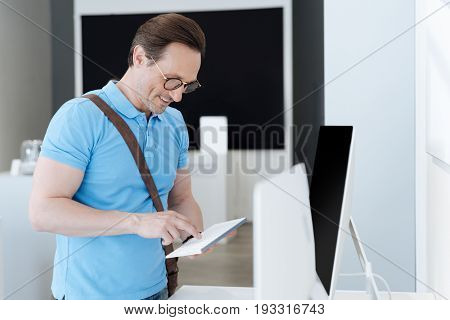 Getting more information. Shot of a brown haired man smiling while standing at a display and typing on a mockup keyboard at an electronics section of a department store.