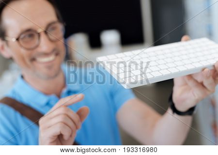 Cannot believe it. Selective focus on a white keyboard held by a smiling adult customer at an electronics section of a department store.