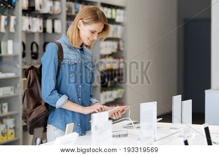 Need to pick up new one. Side view on a female customer standing at a display and using a mockup tablet computer while visiting an electronics store.