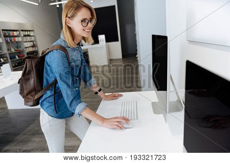  Pretty young woman wearing glasses beaming while trying out a template computer standing on a display while shopping at store.