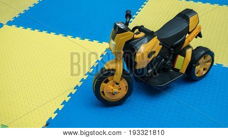 Close Up Of Yellow Motocycle Toy On Rubber Floor With Copy Space At Playground. Cute Little Motocycl