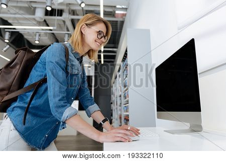  Young lady beaming while shopping for a new personal computer and trying it out while standing at an electronics store display.