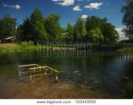 A landscape picture of a lake with sinken bridge and beautifull blue sky with clouds and trees on the background