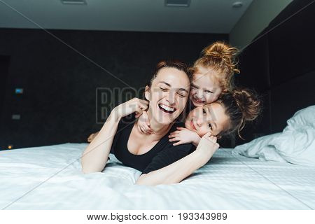 Mom and two daughters have fun on the bed in the bedroom