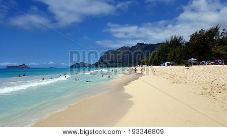 WAIMANALO - MAY 29 2016: Gentle wave lap on Waimanalo Beach as people play in the water looking towards Rabbit island and Rock island on a nice day Oahu Hawaii.