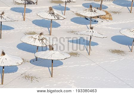Winter on the beach. Frozen beach. Snow on the sand and parasol. Sunshades covered by snow and ice. Novi Sad, Serbia.