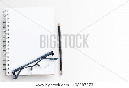 Blank paper notebook and glasses on white table background. Top view with copy space (selective focus). Office desk table concept..Office supplies and gadgets on desk table.Flat lay photo.