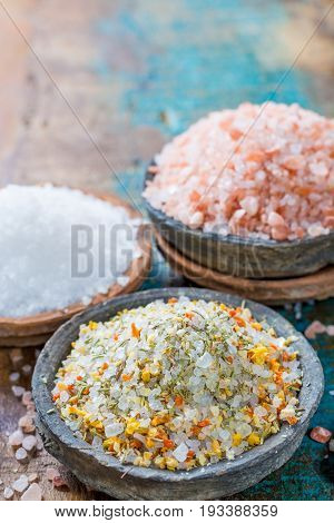Different types of natural salt in stone bowls on wooden surface. White sea salt pink Himalayan salt Spiced salt with rosemary
