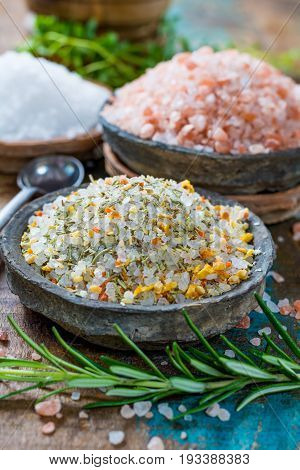 Different types of natural salt in stone bowls on wooden surface. White sea salt pink Himalayan salt Spiced salt with rosemary