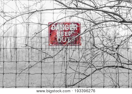 Red Danger Sign Posted To Barbed Fence Tangled In Branches, Warning People To Keep Out
